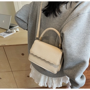 Detail of beige crossbody bag featuring woven texture flap and wavy leather base design