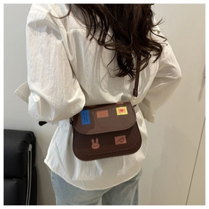 Detail of a brown crossbody bag with creative patches shown from a back perspective