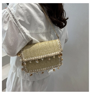 Close-up of straw woven crossbody bag with white crochet lace and seashell charm detail