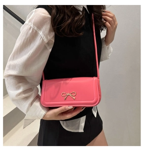 Pink baguette bag with gold bow detail worn by model against a minimalist staircase background