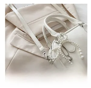 Detailed macro view of white leather bag featuring pearl bow and silver heart pendant charm