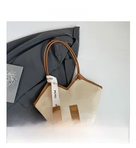 Detail of cream canvas tote bag with brown leather trim and decorative lettered ribbon
