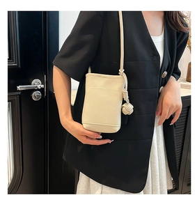 Detail einer beigen Mini-Umhängetasche aus genarbtem Leder mit elegantem Lederknoten-Anhänger