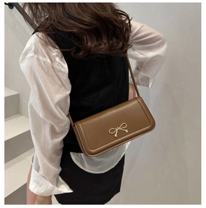 Brown rectangular shoulder bag with golden bow decoration shown on a model
