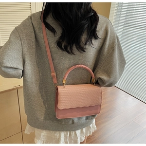 Pink shell handbag with woven texture and wavy edge worn as a crossbody bag