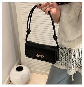 Close-up of black leather underarm bag featuring a stylish golden bow metal buckle