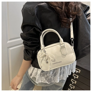 Fashionable white crossbody bag with pearl bow charm shown on model in a modern style