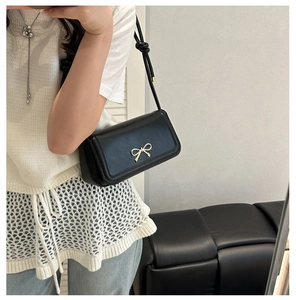Detail of a black leather handbag featuring a golden bow metal buckle on a white outfit