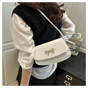 Detailed view of white crocodile texture underarm bag with gold bow clasp on shoulder