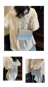 Macro detail of light blue crossbody bag with woven texture lid and golden hardware