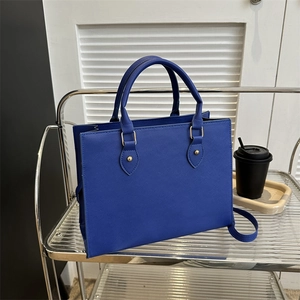 Royal blue Saffiano leather tote bag with gold hardware on a modern minimalist shelf