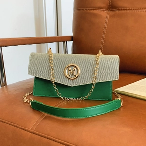 Sac bandoulière rétro en cuir vert avec logo M et chaîne dorée sur fauteuil en cuir
