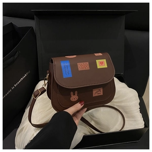 Gros plan du sac besace en cuir PU marron avec écussons rétro colorés dans un coffret