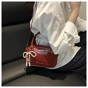 Detail of burgundy crossbody bag with glossy finish and decorative pearl bow charm