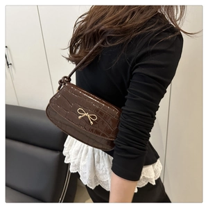 Detail of dark brown croc-effect shoulder bag with a gold bow buckle on a model