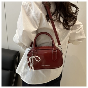 Detail of burgundy glossy bowling bag with pearl bow charm and white fashion logo