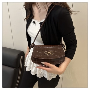 Detail of dark brown crocodile embossed texture and golden bow buckle on a crossbody bag