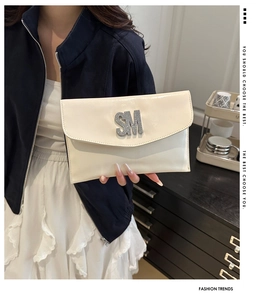 Close-up of cream patent leather clutch featuring a silver SM metal logo and flap design