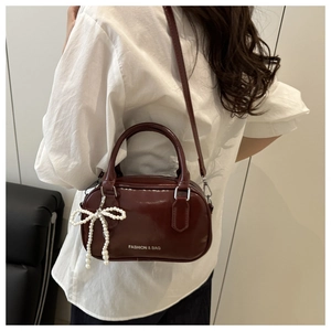 Detail of burgundy glossy handbag featuring pearl bow charm and white fashion text