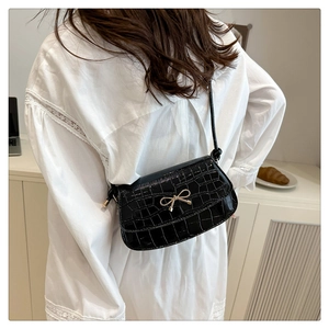Detail of black crocodile embossed shoulder bag with gold bow clasp on a female model