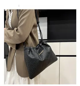 Dettaglio ravvicinato di una borsa a tracolla nera intrecciata con logo dorato e coulisse