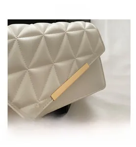 Detail of white quilted crossbody bag featuring triangular patterns and gold metal clasp