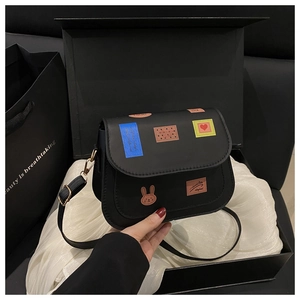 Détail du sac besace noir avec écussons colorés présenté dans un coffret cadeau