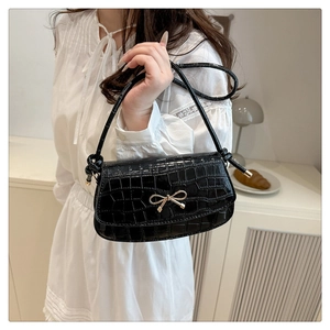 Detailed close-up of black crocodile pattern shoulder bag with golden bow hardware