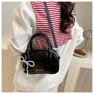 Detail of black glossy pillow bag featuring pearl bow charm and white fashion lettering