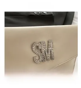 Macro detail of cream leather bag with rhinestone SM metal logo and precision stitching