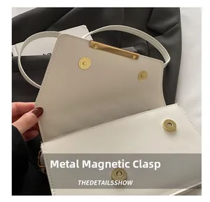 Detail of white envelope bag featuring dual gold magnetic buckles and metallic trim