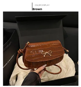Dettaglio della borsa a tracolla marrone con motivo coccodrillo e fiocco dorato in box