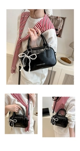 Detail of black glossy handbag with pearl bow charm and detachable shoulder strap