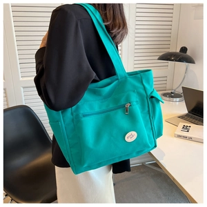 Detail view of turquoise canvas tote bag with front zipper and Good Luck embroidery
