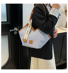 Detail of blue denim tote bag with V-shaped opening and brown leather trim on the shoulder