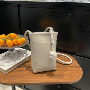 Schicke kleine Handytasche aus cremefarbenem Leder mit Knotenanhänger auf Holztisch