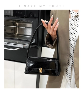 Detail of black glossy patent leather underarm bag with a gold metal buckle on flap
