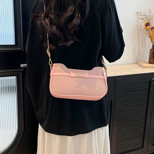 Pink quilted crossbody bag with bow detail shown on model in a stylish indoor setting