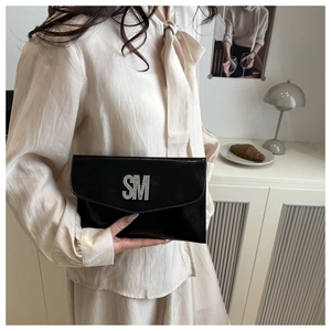 Detail view of a black glossy clutch bag featuring a sparkling rhinestone SM metal logo
