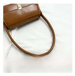 Close-up of brown patent leather shoulder bag featuring a gold twist lock and smooth strap