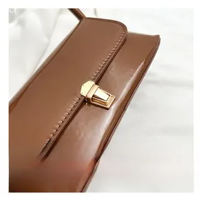 Close-up of brown patent leather bag with a gold metal push-lock and stitching details