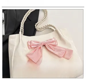 Detail of a cream tote bag with pink satin bow and woven rope handles