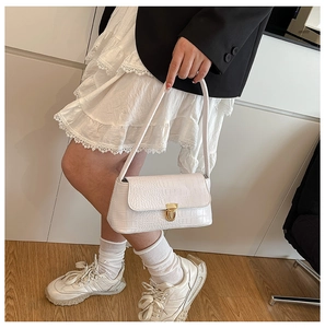 Detail of white crocodile texture underarm bag featuring a gold clasp on a leather strap