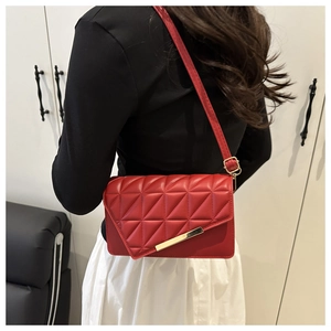 Detail of red quilted crossbody bag featuring gold metal trim and adjustable strap on a model