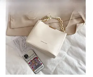 Detail of a minimalist cream leather bucket bag with gold hardware and acrylic chain
