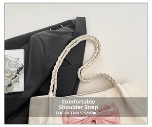Detail of woven shoulder strap and pink ribbon bow on off-white tote bag