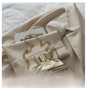 Detail of cream drawstring bucket bag with gold chain strap and pearl charm accent