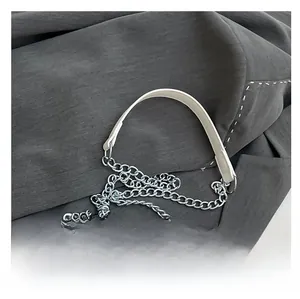 Detail of cream woven handbag showing silver chain strap and metal clasp on gray fabric