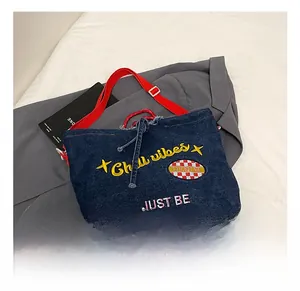 Detail of blue denim tote bag with Chill Vibes embroidery and red adjustable strap