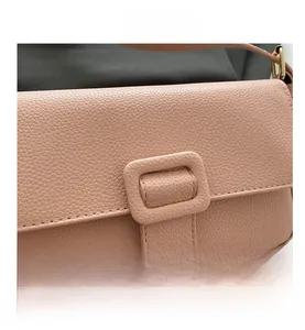 Close-up of litchi grain leather texture and metallic square buckle on pink crossbody bag